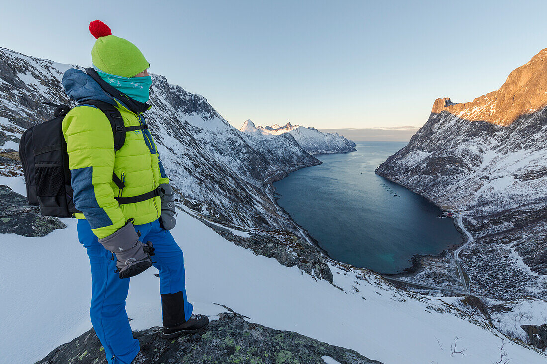 Wanderer auf dem Kamm bewundert das Dorf Fjordgard umrahmt von dem gefrorenen Meer des Ornfjorden, Senja, Troms, Norwegen, Skandinavien, Europa