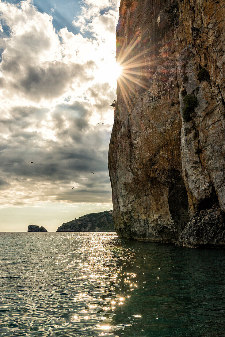 Italien, Kampanien, Cilento, Sonne verschwindet hinter Klippe auf dem Meer