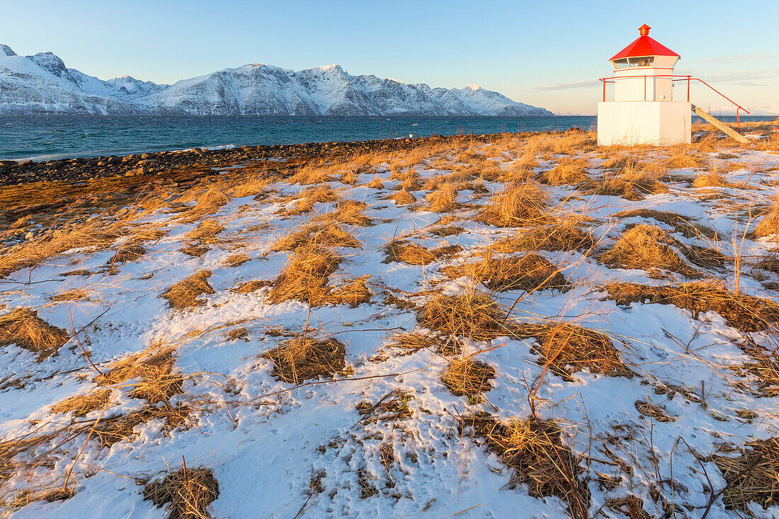 The sun illuminates the coast near a traditional lighthouse, Spaknesora naturreservat, Djupvik, Lyngenfjord, Lyngen Alps, Troms, Norway, Lapland, Europe