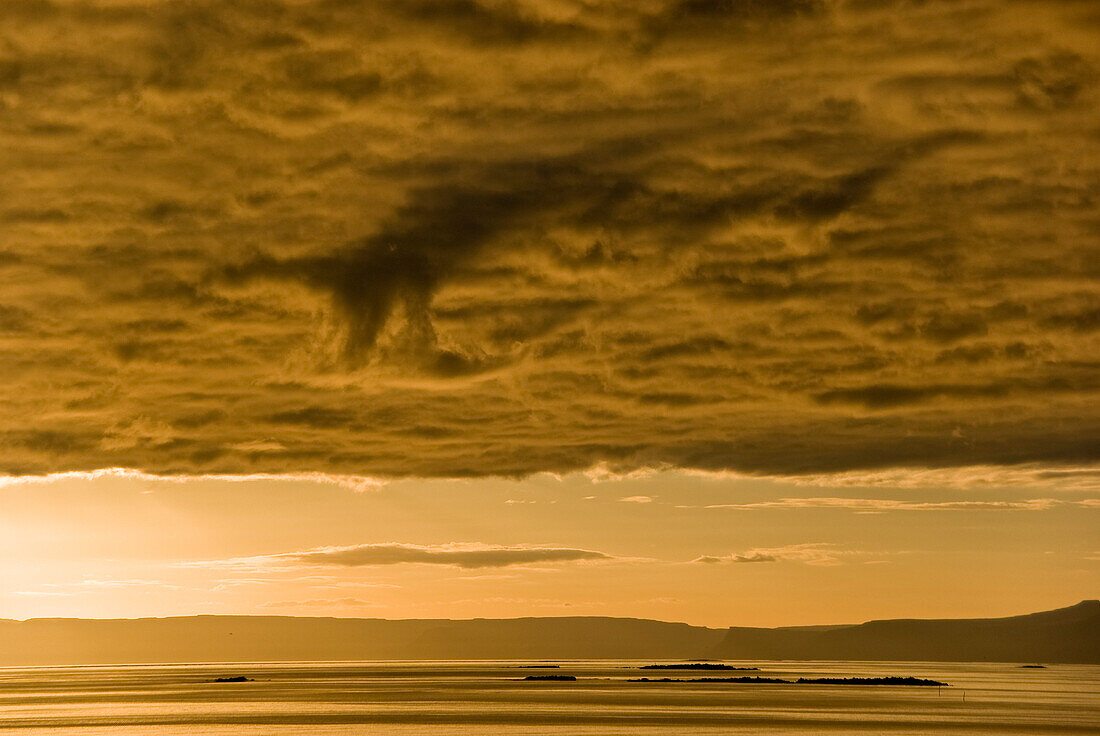 Sunset whit orange light over the ocean that is surmounted by a layer of low clouds, Flatey island, Iceland