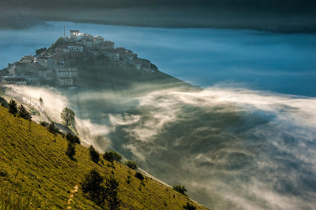 Die Stadt Castelluccio di Norcia im Nebel bei Sonnenuntergang, Monti Sibillni NP, Umbrien, Italien