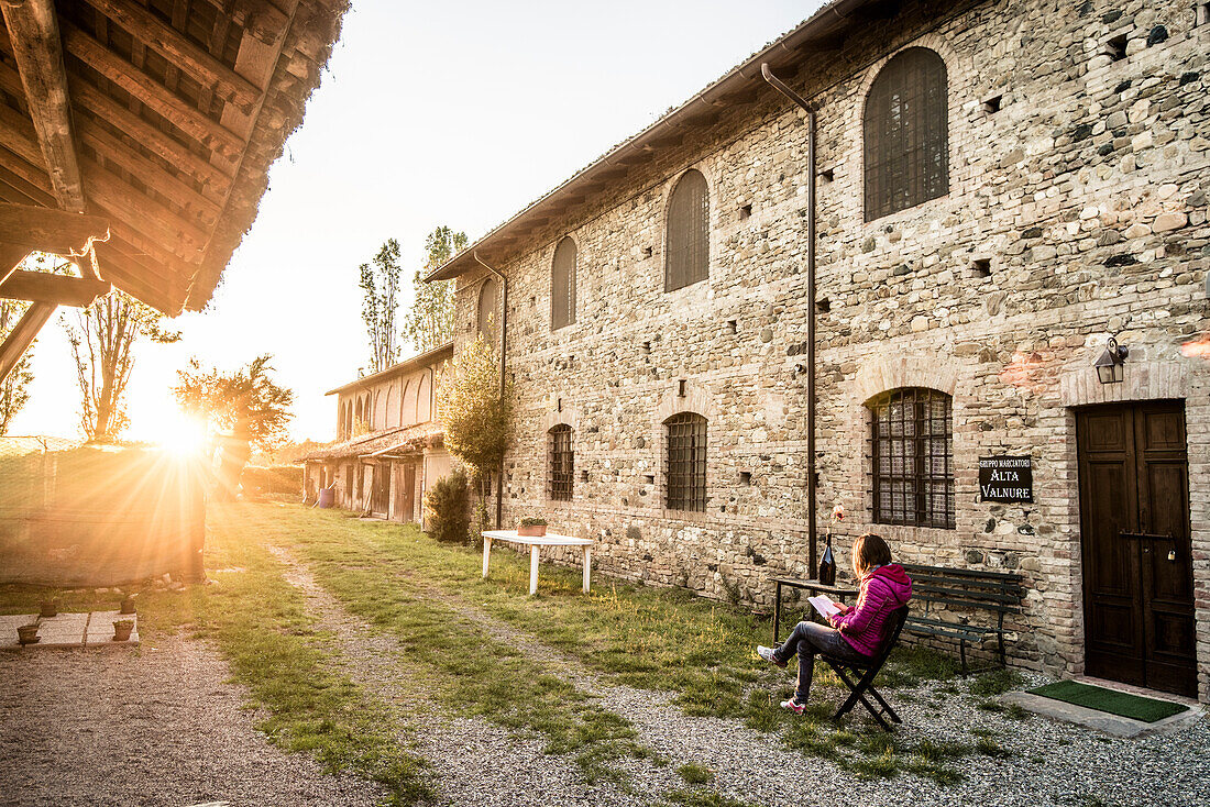Grazzano Visconti, Vigolzone, Piacenza Bezirk, Emilia Romagna, Italien, Frau liest auf einem Stuhl in einem alten Hof der Stadt