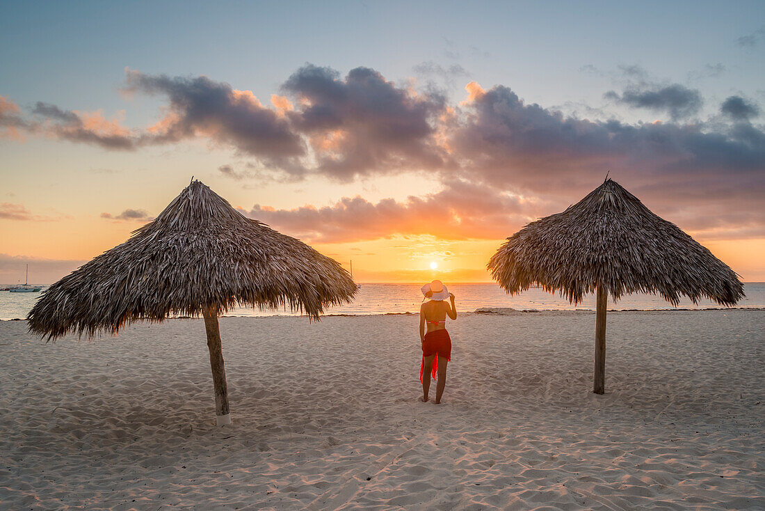 Bavaro Beach, Bavaro, Higuey, Punta Cana, Dominikanische Republik, Frau von thatch Sonnenschirme am Strand bei Sonnenaufgang, MR