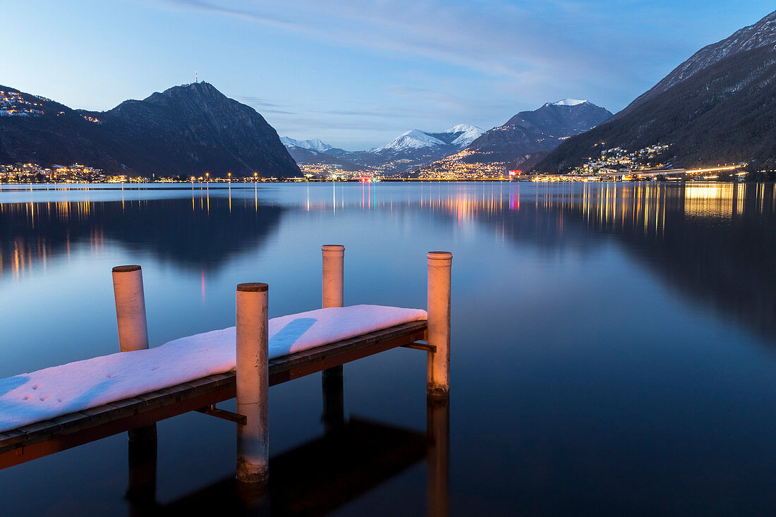 Evening lights of Lugano and Campione d'Italia in front of a pier on Lake Ceresio, Riva San Vitale, Canton Ticino, Switzerland