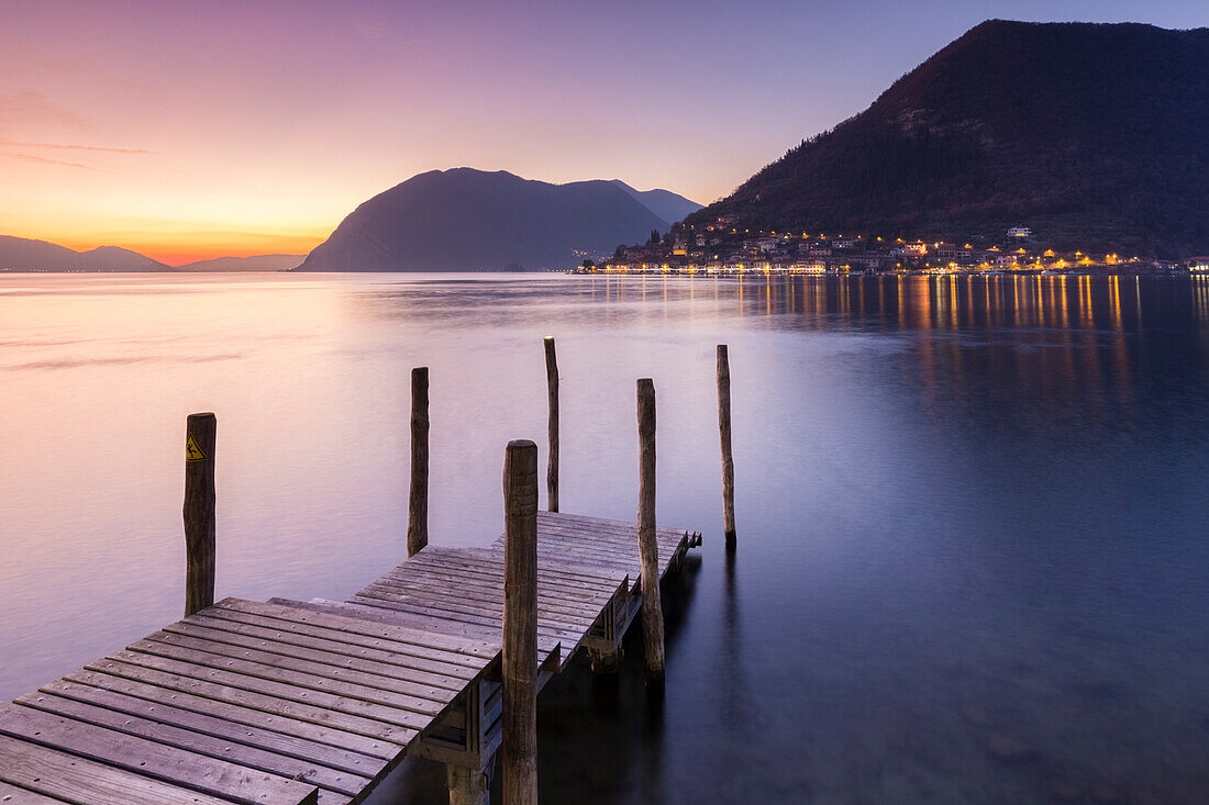 Ein Pier in Sulzano, vor Montisola und Peschiera Maraglio Stadt während eines Wintersonnenuntergang, Provinz Brescia, Iseosee, Lombardei, Italien