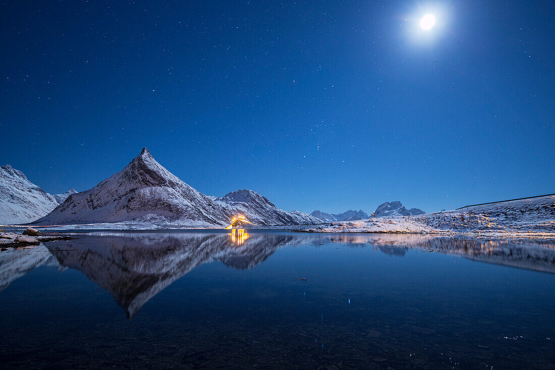 Full moon and stars light up the snow capped peaks reflected in sea Volanstinden Fredvang Lofoten Islands Northern Norway Europe