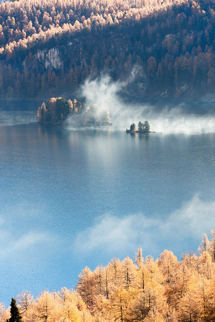 Nebel über dem blauen See Sils und die bunten Wälder des Herbstes Maloja Kanton Graubünden Engadin Schweiz Europa