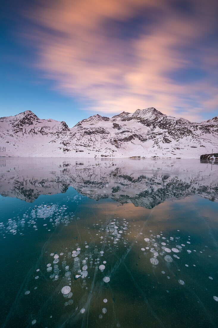 Eisblasen und rosa Wolken bilden den gefrorenen Lago Bianco im Morgengrauen Bernina Pass Kanton Graubünden Engadin Schweiz Europa