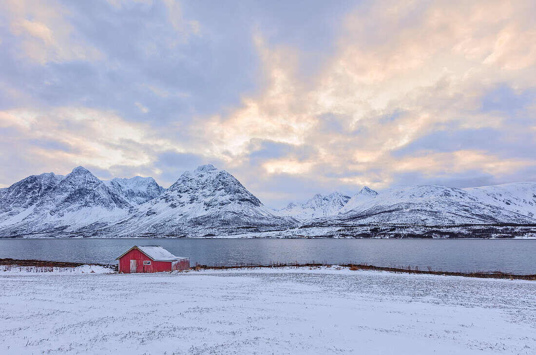 Typische Rorbu in der verschneiten Landschaft umgeben von den gefrorenen Meer und hohen Gipfeln Svensby Lyngen Alpen Tromsø Norwegen Europa