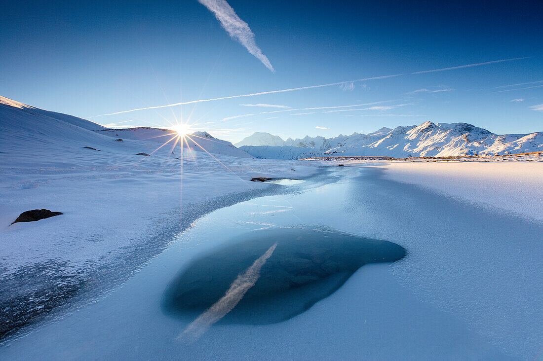 Rays of sun on the frozen Lake Piz Umbrail framed by Mount Ortles in background Braulio Valley Valtellina Lombardy Italy Europe