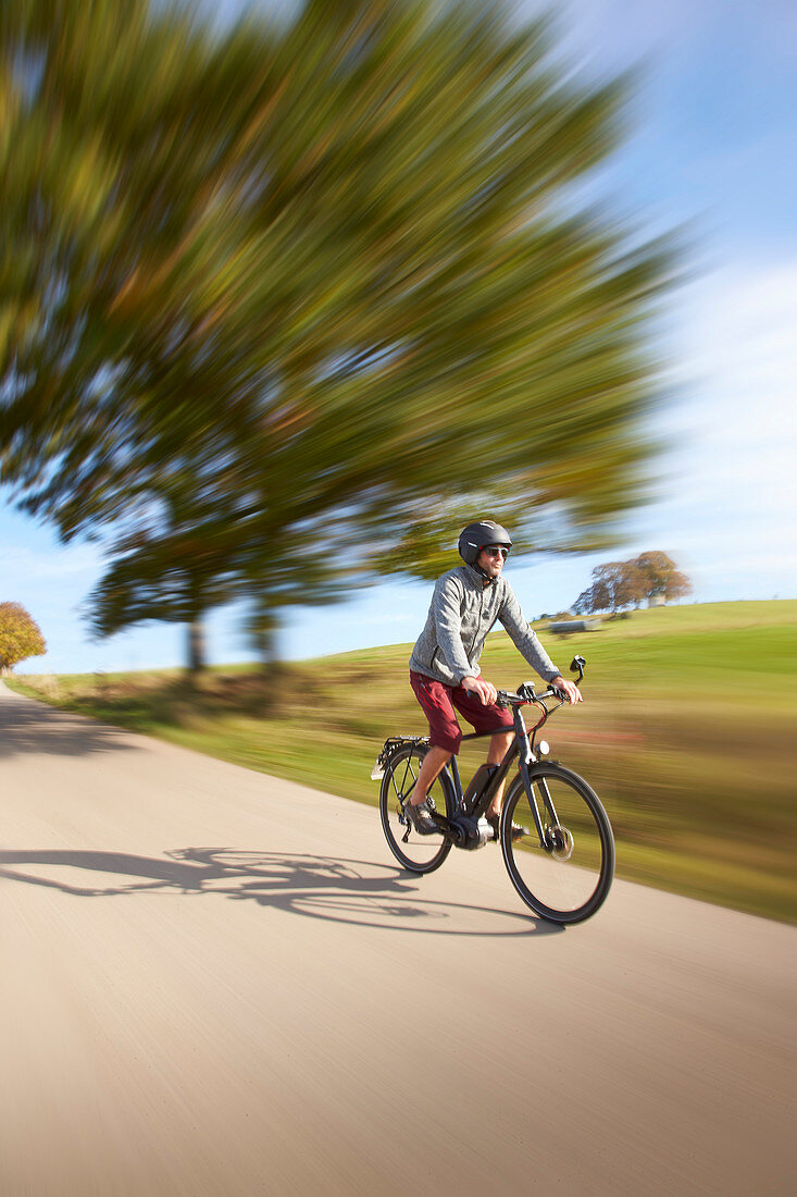 Cyclist on an e-bike on a country road, Muensing, Upper Bavaria, Germany