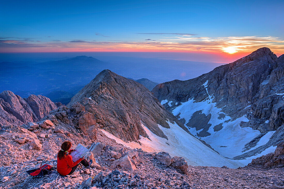 Frau beim Wandern sitzt bei Sonnenaufgang am Corno Grande, Blick auf Gran Sasso-Gruppe, Corno Grande, Gran Sasso, Abruzzen, Italien