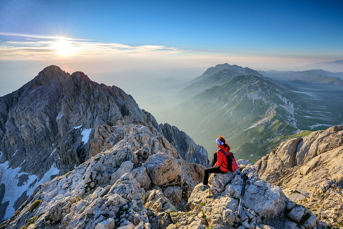 Frau beim Wandern sitzt bei Sonnenaufgang am Corno Grande, Blick auf Gran Sasso-Gruppe, Corno Grande, Gran Sasso, Abruzzen, Italien