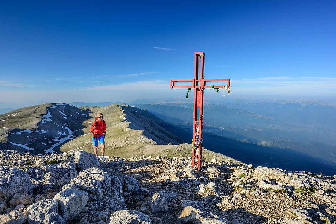 Woman hiking ascending towards cross at summit of Monte Amaro, Monte Amaro, Majella, Abruzzi, Italy