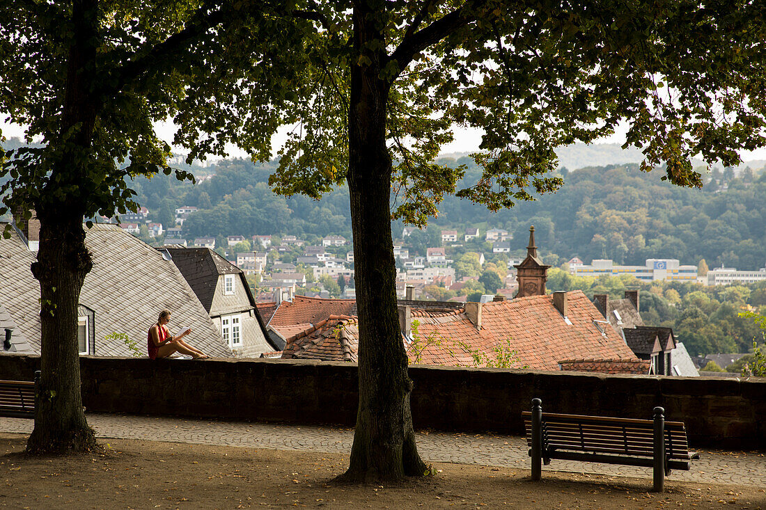 Female student sits on wall at the Lutheran churchyard with a view over the city, Marburg, Hesse, Germany, Europe