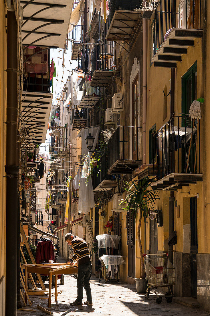In einer Gasse mit Balkonen arbeitet ein Handwerker, Via Orologio, Palermo, Sizilien, Italien, Europa