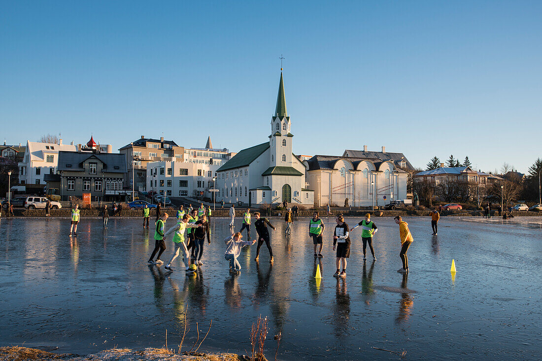 School children play soccer on frozen Tjörnin lake with Fríkirkjan (Frikirkjan) church behind, Reykjavik, Iceland, Europe