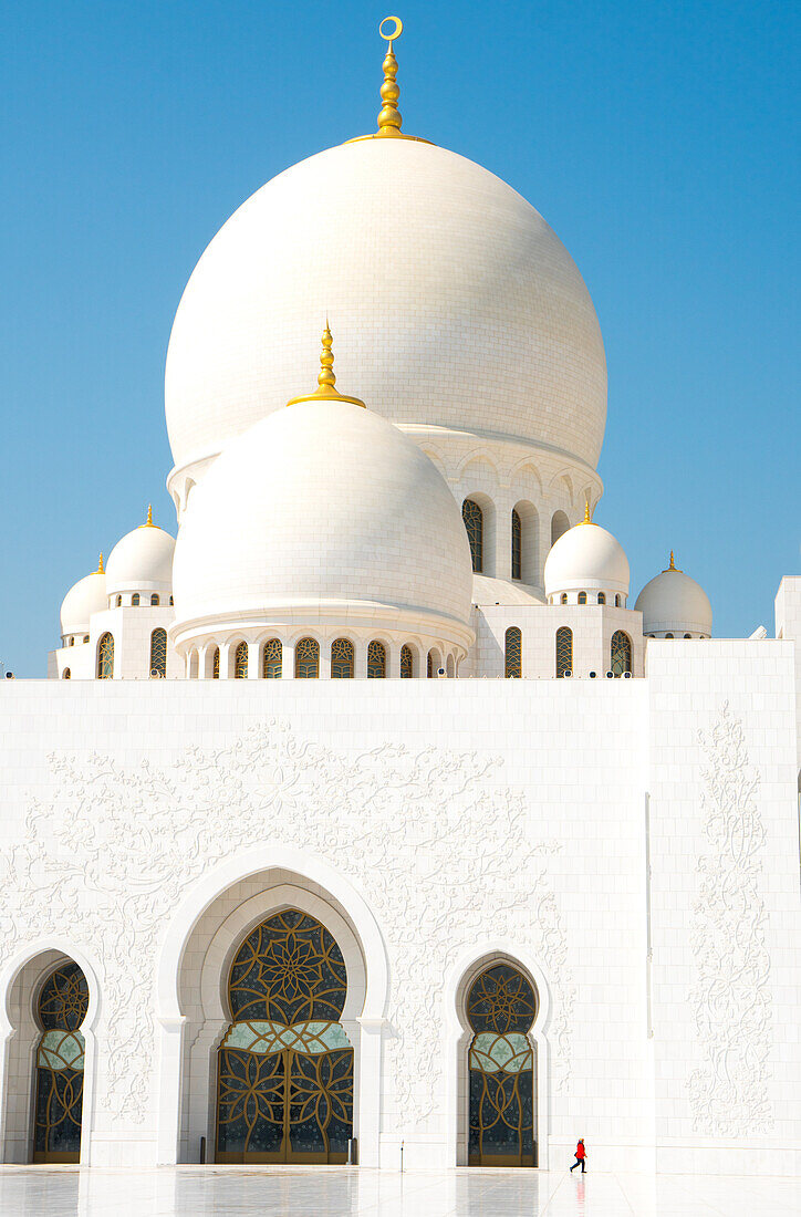 Interior of Sheikh Zayed Grand Mosque, brilliant white of marble buildings punctuated by tiny woman in red, Abu Dhabi, United Arab Emirates, Middle East