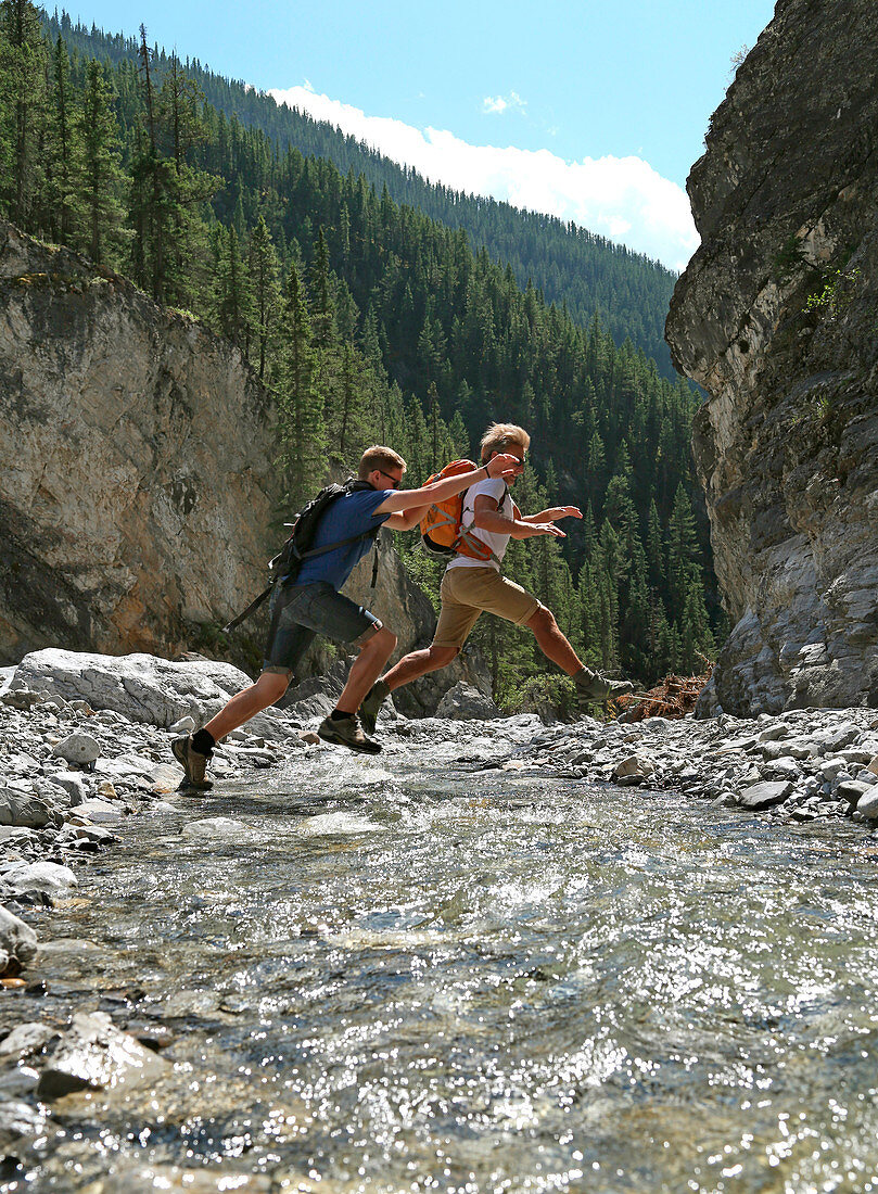 Father and son jumping across mountain river