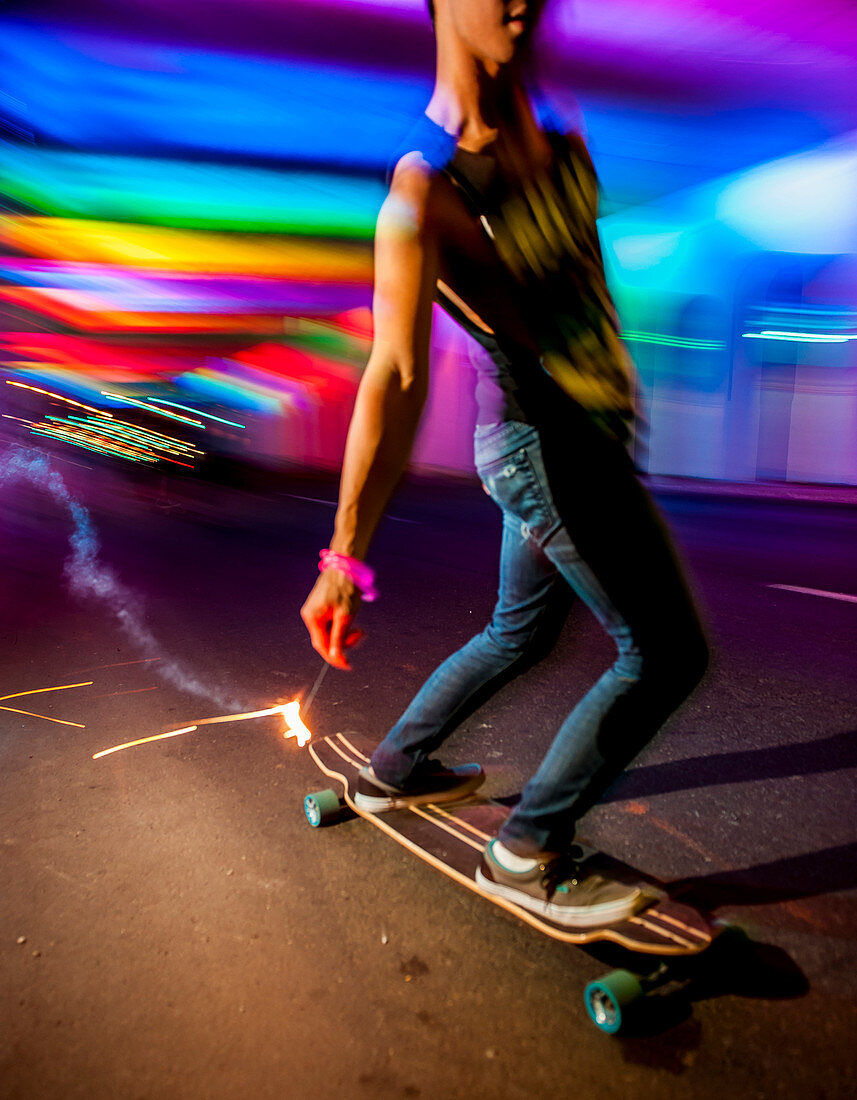 Young man skateboarding in lit traffic tunnel with sparkler in hand