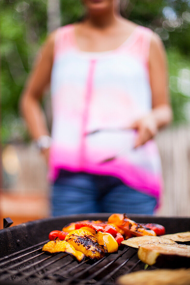 A Japanese American women grills colorful vegetables on a charcoal grill in the backyard.