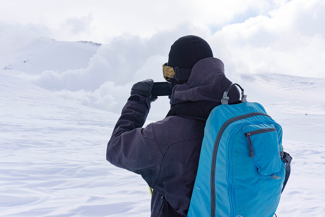Ein Snowboarder, der ein Bild auf seinem Telefon der Rauchlöcher auf dem Berg hat. Asahi