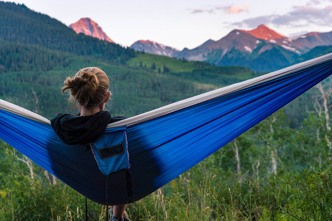 Young female in hammock looking at mountain peaks during sunset