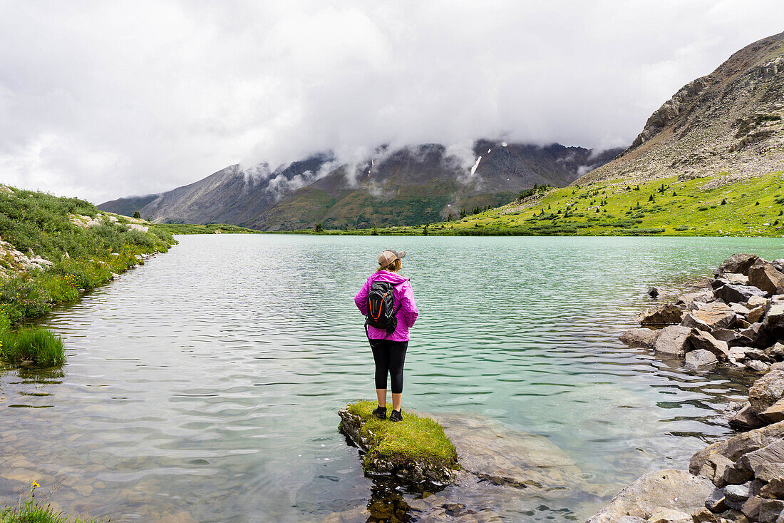 Young female stands on rock in a high alpine lake in Colorado