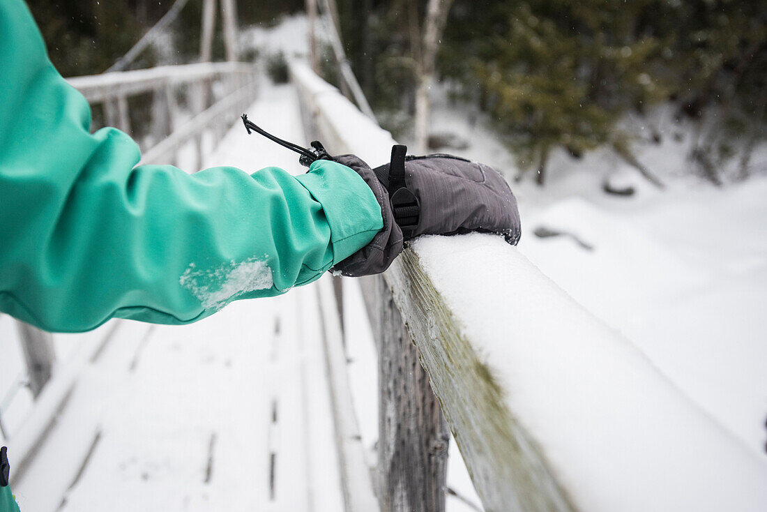 Person hiking acrossÂ footbridgeÂ in winter