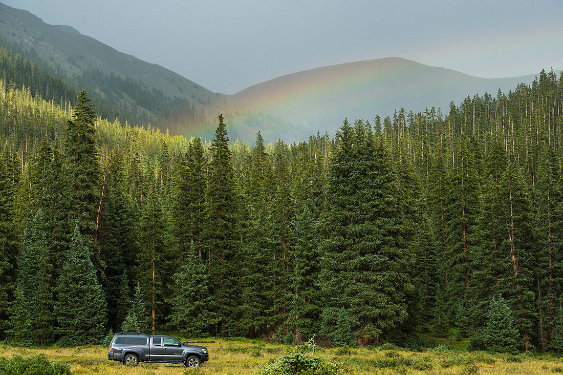 A backcountry mountain scene with a truck and a rainbow overhead