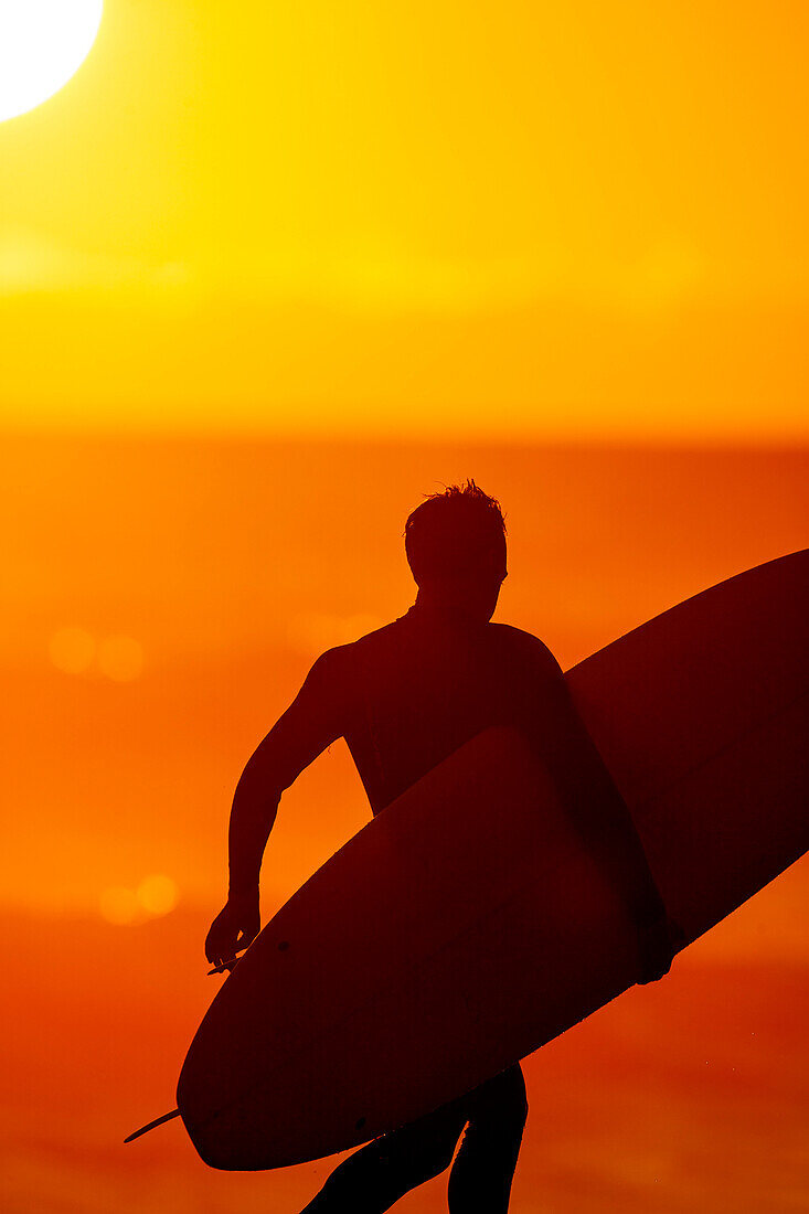 Nahaufnahme eines Mannes mit Surfbrett am Sonnenuntergang