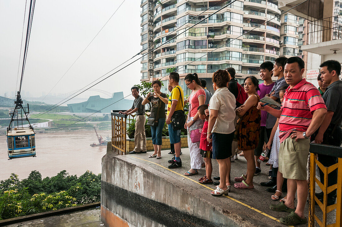 'Passagiere warten auf die Seilbahn für den Übergang Yangtze River in Chongqing, die Stadt als Hintergrund von der Nebel bedeckt; Chongqing, China'