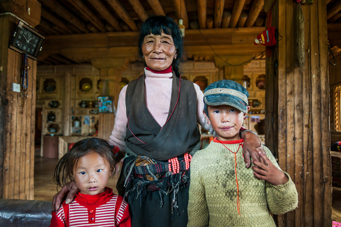 'Innerhalb eines traditionellen tibetischen Hauses, großes Wohnzimmer, wo eine alte Frau und ihre Enkel für ein Foto posieren; Daocheng, Provinz Sichuan, China'