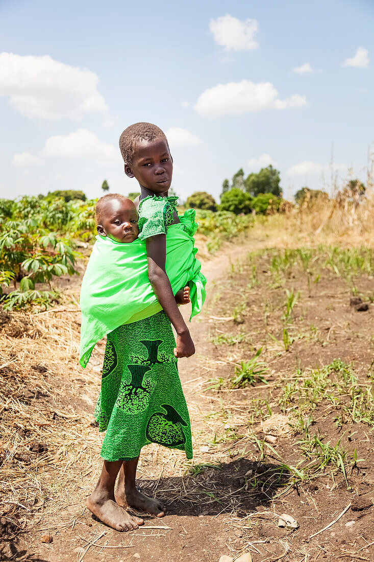 'Ein junges Mädchen trägt ein Baby auf dem Rücken in einer Schlinge; Uganda'