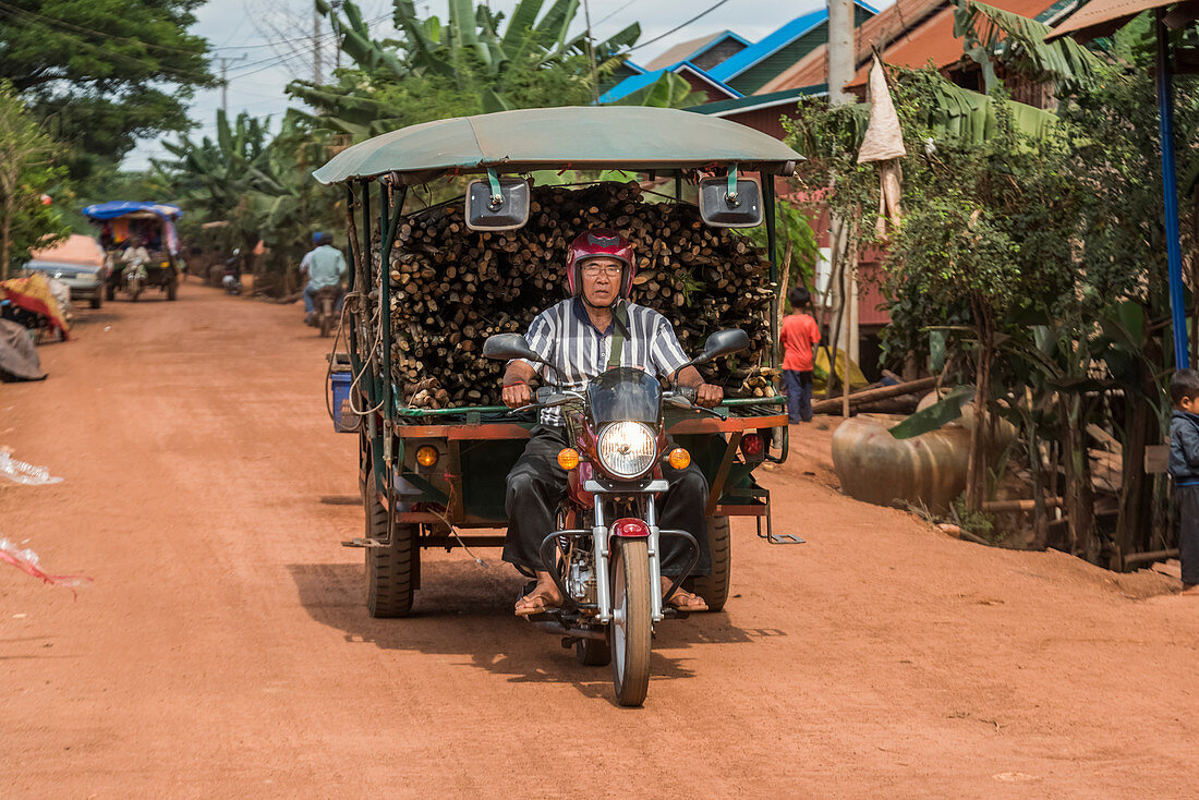 Ein Mann reitet ein Motorrad, das einen Wagen mit geschnittenem Holz zieht. Siem Reap Provinz, Kambodscha