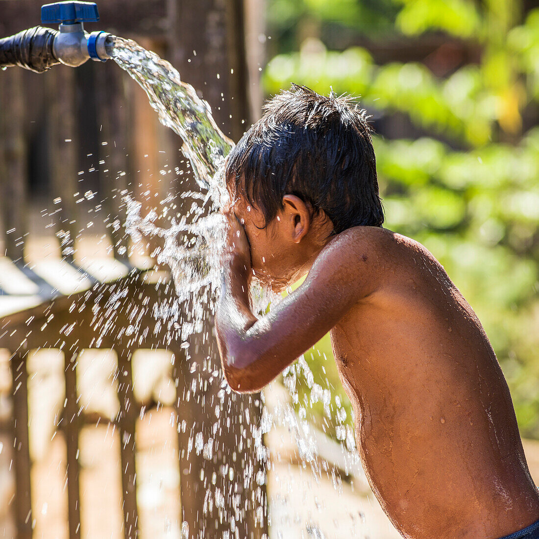'Ein Junge steht unter einem Hahn und reinigt sein Gesicht mit dem Spritzwasser, Kamu Dorf; Tambon Po, Chang Wat Chiang Rai, Thailand'