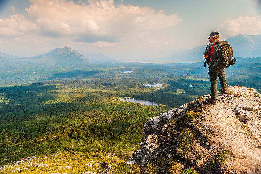 Backpacker overlooks scenic view from a bluff high above, Wrangell-St. Elias National Park, Southcentral Alaska, USA