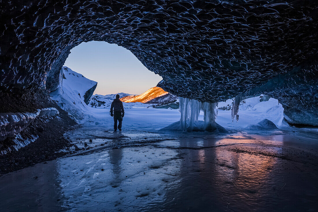 'A man walks out the entrance of an ice tunnel at the terminus of Canwell Glacier in the Alaska Range in mid-winter; Alaska, United States of America'