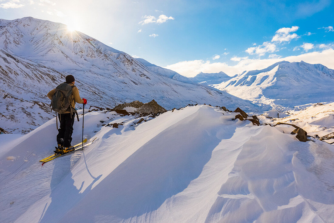 'A backcountry skier looks over the Black Rapids Glacier valley from a high point on the terminal moraine in winter; Alaska, United States of America'