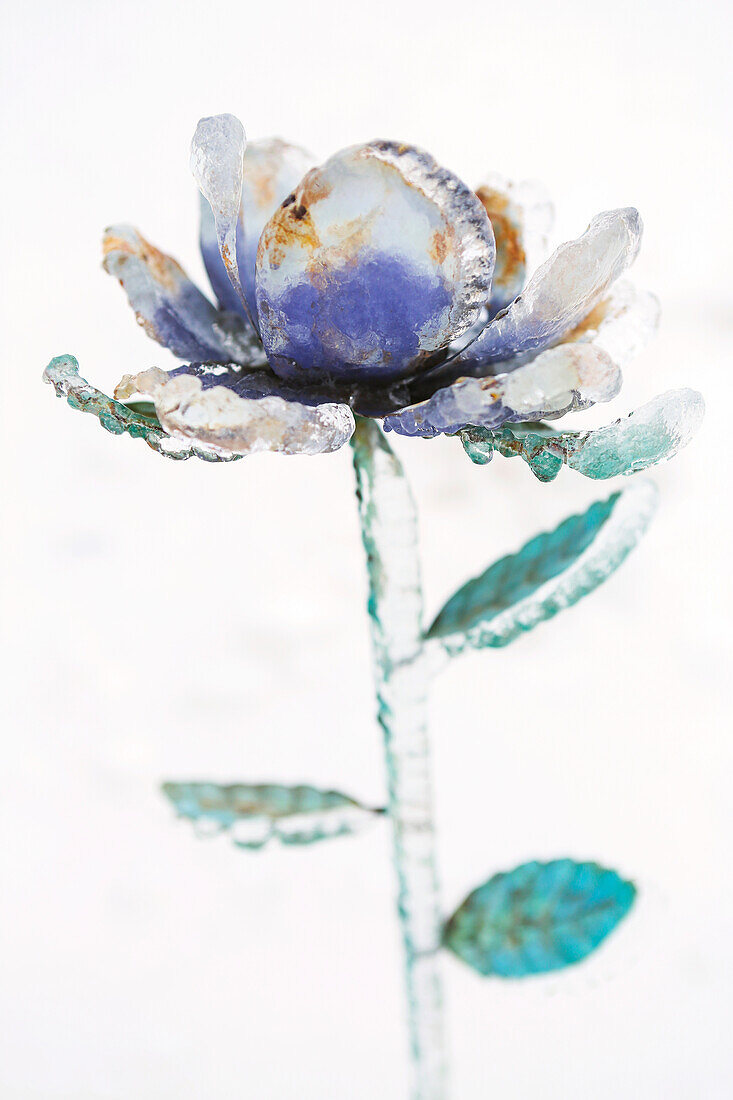 A metal flower encased in ice from an ice storm against a white background