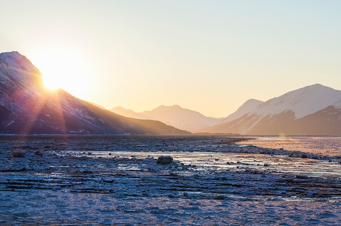 'Sunrise peaks over the Chugach Mountains into Turnagain Arm on an icy winter morning; Alaska, United States of America'