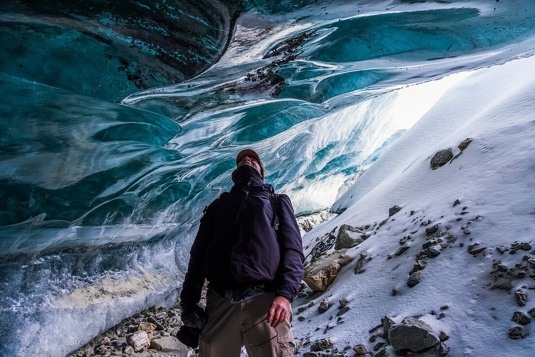 'A man looks up at the ice of Canwell Glacier while standing in the entrance to an ice cave; Alaska, United States of America'