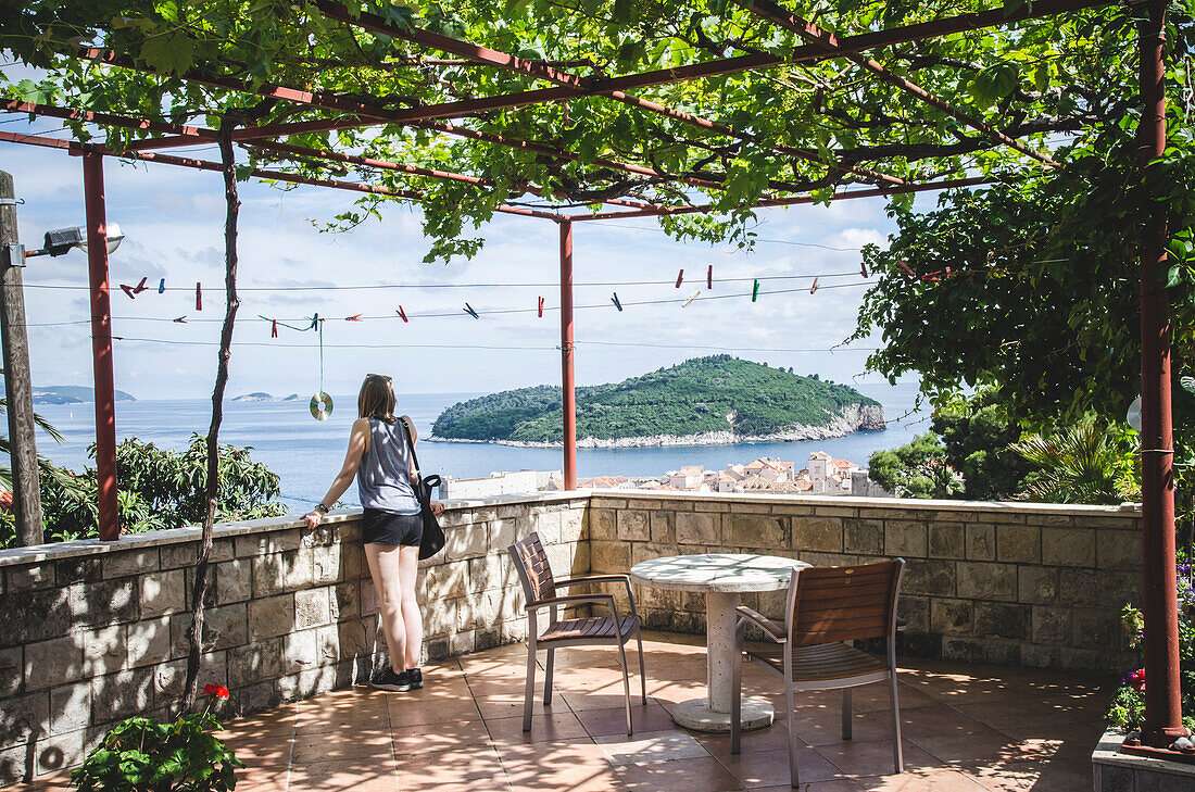 Young Woman on Covered Patio Looking Out Over Dubrovnik with Lokrum Island in Distance, Croatia