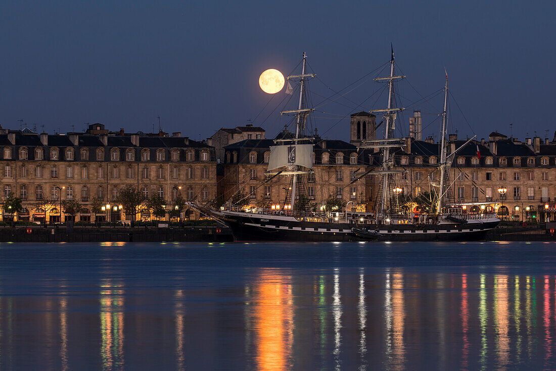 Das Segelschiff Belem auf Fluss Garonne am Pier mit Blick auf die französischen Häuserfassaden der Quai Richelieu mit Mondaufgang in der Abenddämmerung, Bordeaux, Gironde, Nouvelle-Aquitaine, Frankreich, Europa