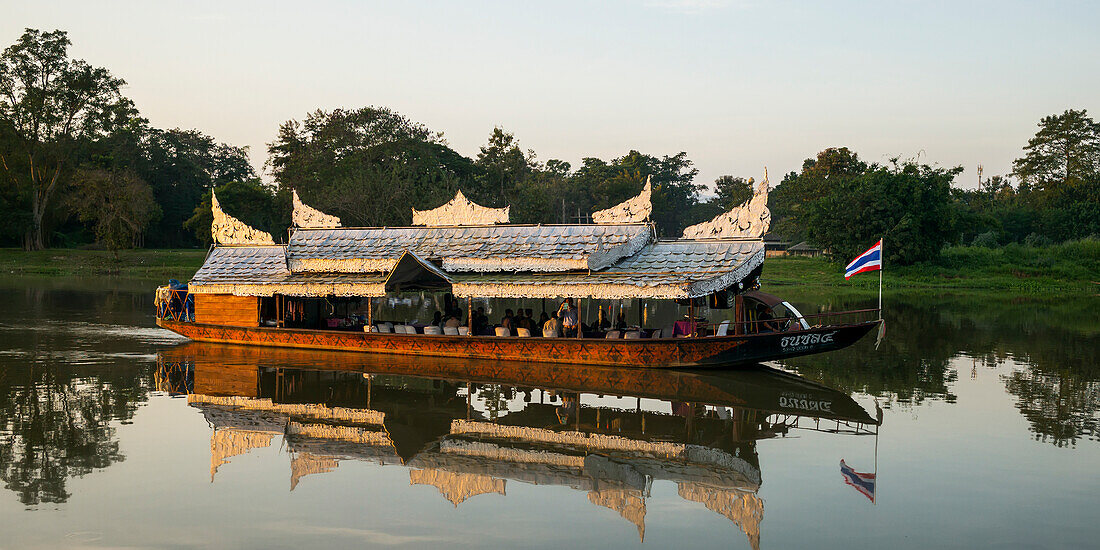 Ein Tourboot segelt langsam einen ruhigen Fluss hinunter. Chiang Rai, Thailand