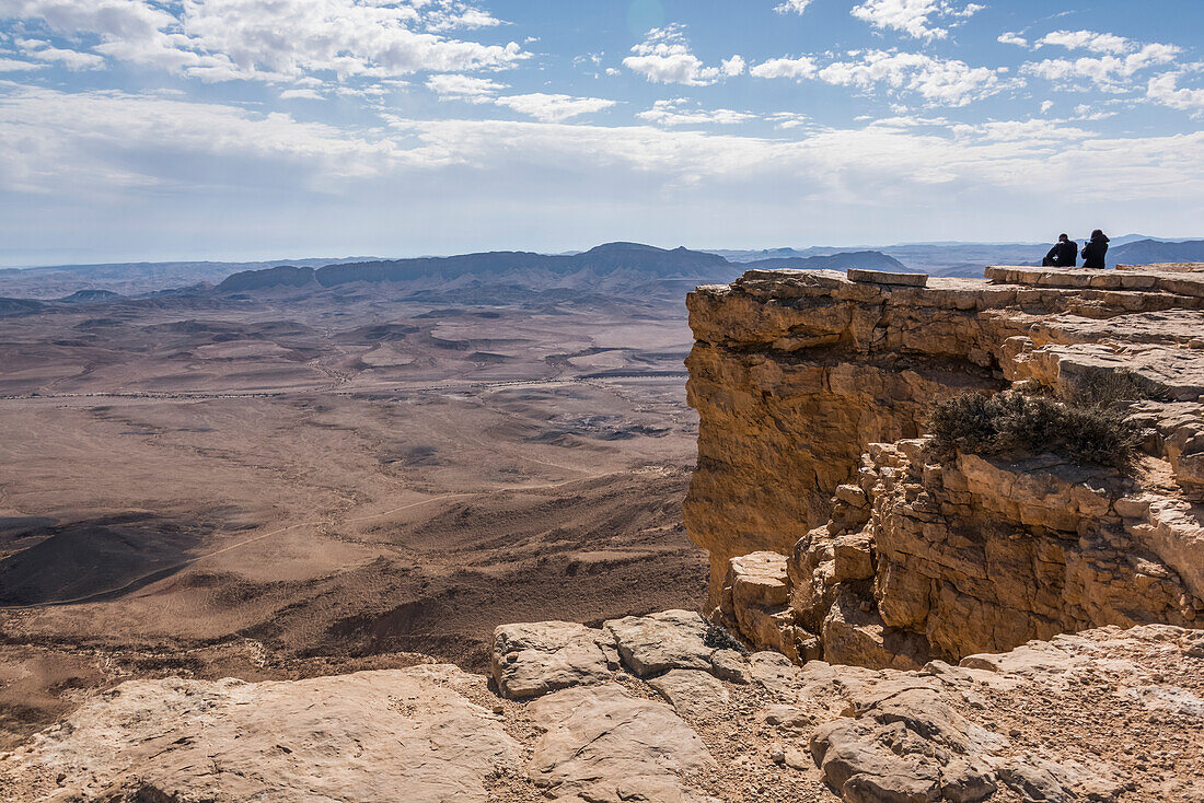 'People standing on a rock ridge looking out at the view of the rugged landscape, Ramon Nature Reserve; Mitzpe Ramon, South District, Israel'