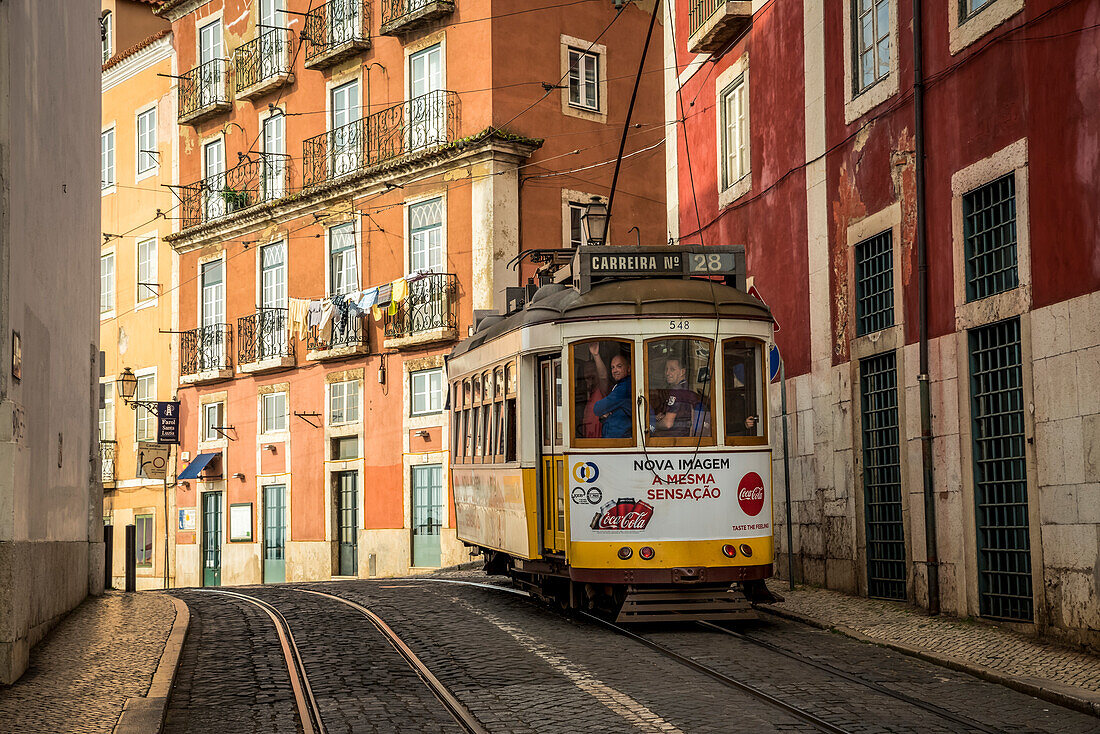 'A tram travels down the tracks beside buildings, Alfama; Lisbon, Portugal'