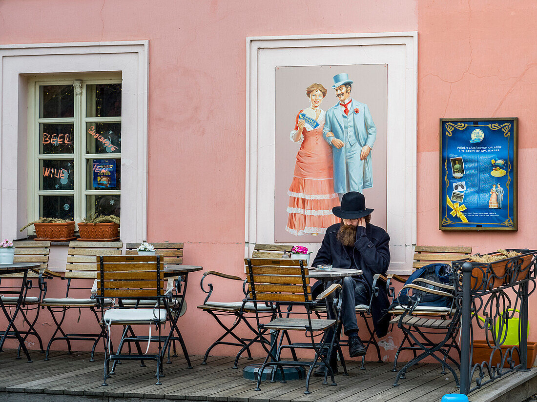 'Ein Mann sitzt allein auf einer Außenterrasse eines Cafés; Prag, Tschechische Republik'