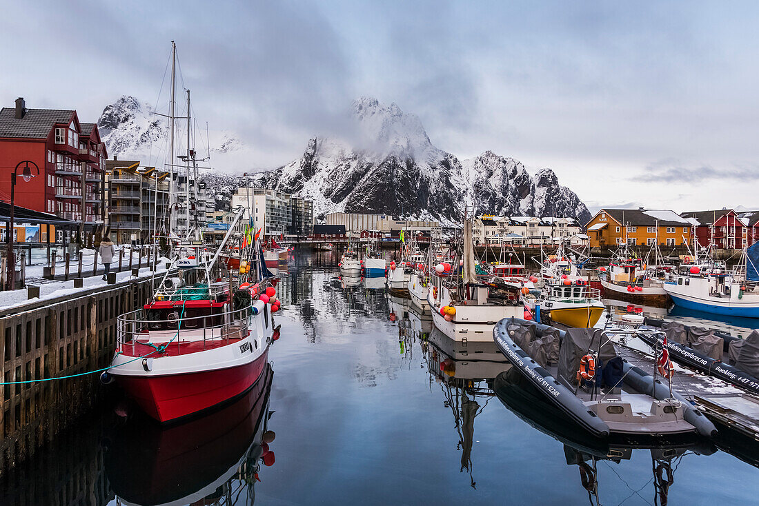 'Boats moored in a harbour with rugged mountains along the coastline; Svolvar, Lofoten Islands, Nordland, Norwa'