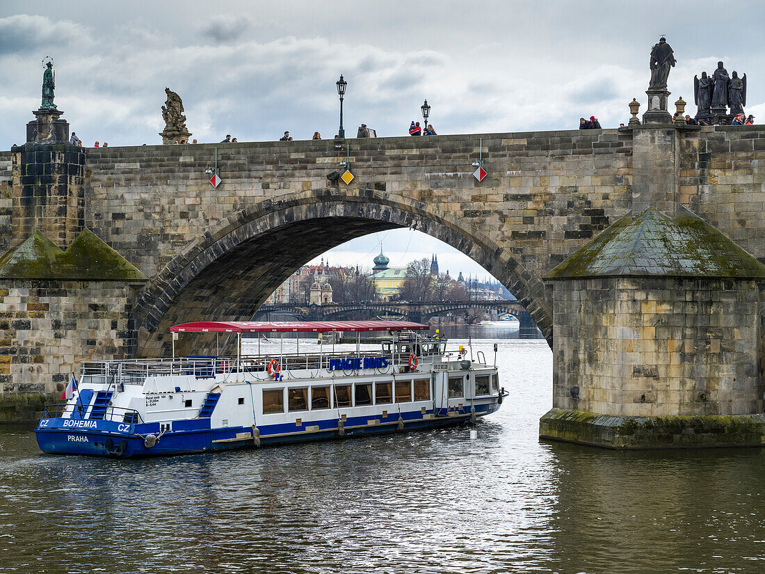 'A tour boat passing under Charles Bridge on the Vltava River; Prague, Czech Republic'